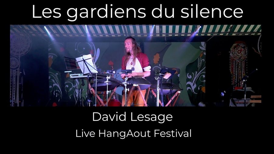 Scène de festival éclairée de bleu et de violet : l’artiste debout derrière ses instruments, un pupitre devant lui ; titre incrusté « Les gardiens du silence — David Lesage, Live HangAout Festival ».