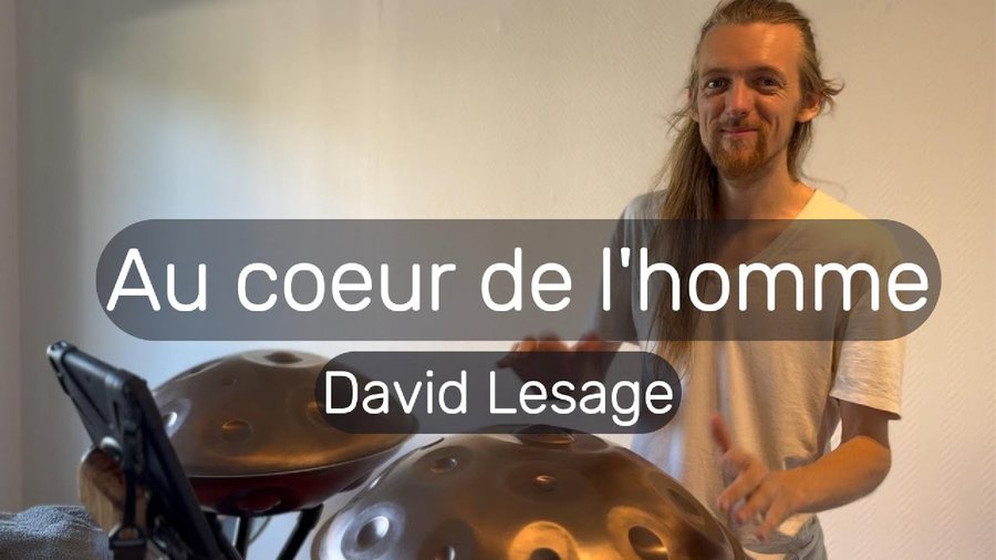 L’artiste debout derrière deux handpans acoustiques en métal clair posés sur pieds, dans une pièce claire ; titre incrusté « Au cœur de l’homme ».
