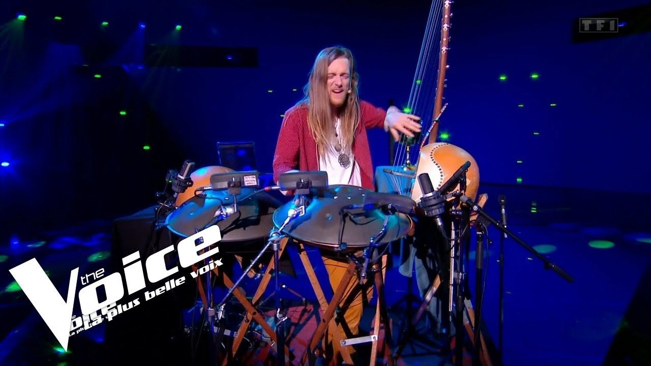 Vignette de la vidéo : David Lesage seul sur le plateau bleu de The Voice, un micro serre-tête au visage, entouré de ses handpans sur pieds, de son N’Goni 14 cordes et d’une calebasse. Logos The Voice et TF1 incrustés.