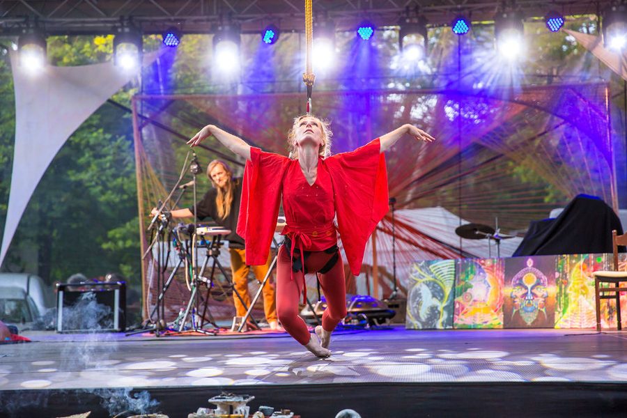 Iris Chasles en tenue rouge, bras ouverts et regard vers le haut, suspendue à un élastique sur la scène en plein air de l’Everness Festival ; derrière elle, David Lesage joue debout à ses machines.