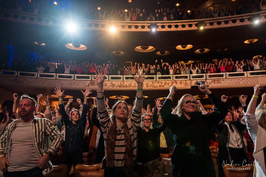 La mise en mouvement de la respiration de la joie de 2 700 personnes, guidée par Iris Chasles : la salle du Grand Rex debout, au premier rang les bras tendus vers la scène ; derrière, les deux balcons pleins jusqu’en haut, découpés par les projecteurs.