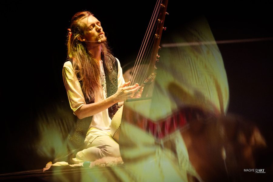 David Lesage, à genoux et micro-casque au visage, joue du ngoni dans une lumière vert et or ; au premier plan, le mouvement flou d’une danseuse traverse le cadre.