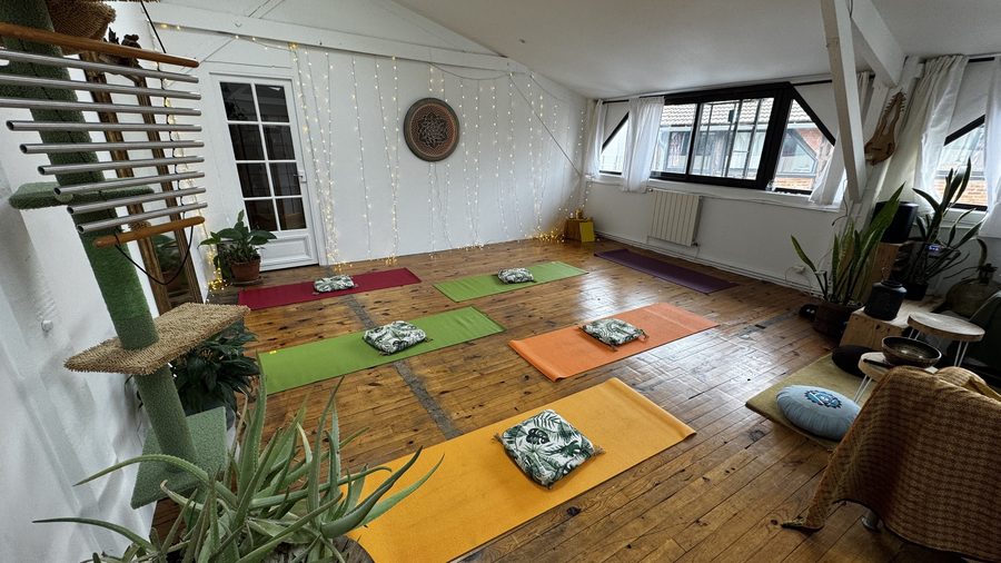 La salle du Nid avant un atelier : des tapis de yoga colorés et des coussins disposés sur le parquet, un rideau de guirlandes lumineuses et des plantes