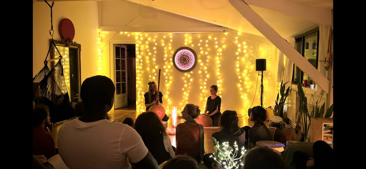 Une soiree au Nid : le public assis au sol devant un rideau de guirlandes lumineuses, deux musiciennes et des bougies