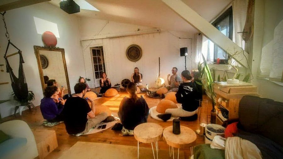 Workshop rythme à la calebasse : une dizaine de personnes assises en cercle au sol autour de calebasses, dans la pièce mansardée du Nid