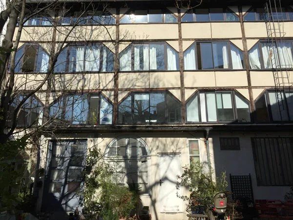 Façade vitrée du Nid, ancien atelier d’artiste sur trois niveaux, vue depuis la cour pavée plantée.